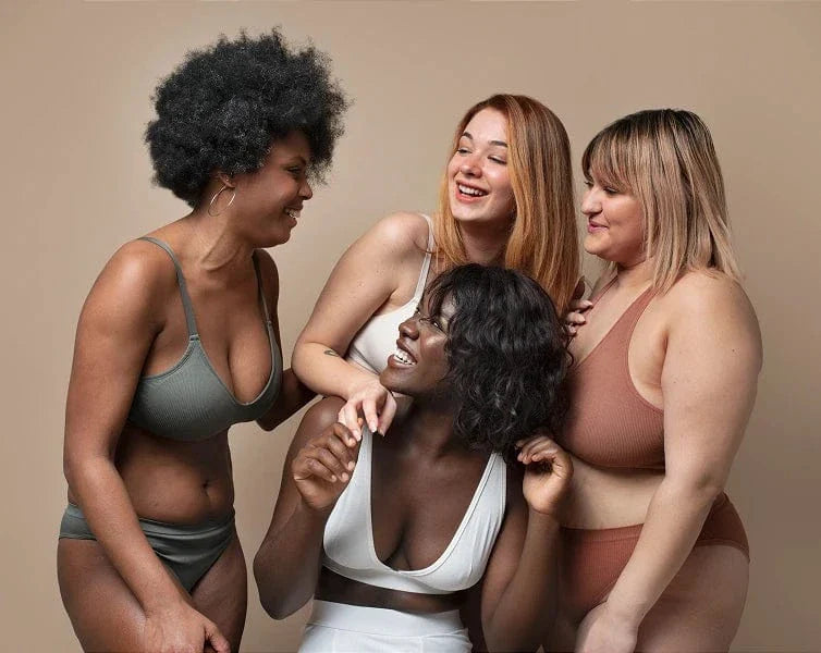 Four women in various stages of undress standing close together against a beige background
